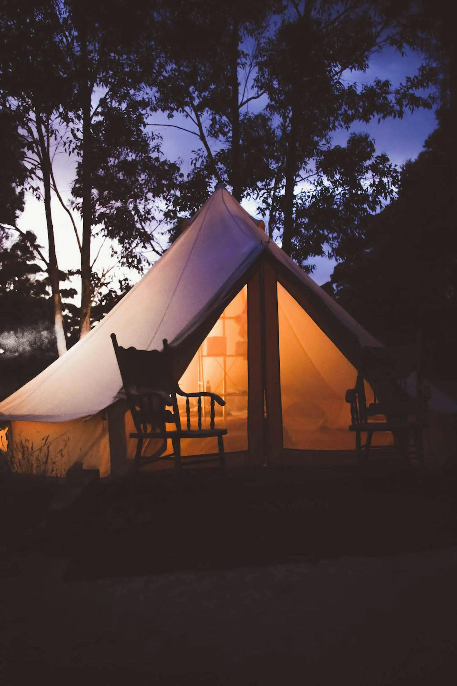 Experience a serene glamping setup with glowing tent amidst Australian woods at dusk.