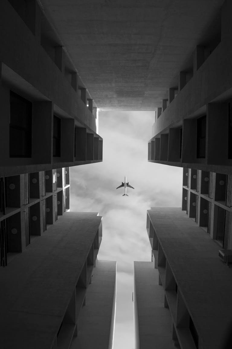 Low angle of symmetrical buildings against sky with airplane. Monochrome.