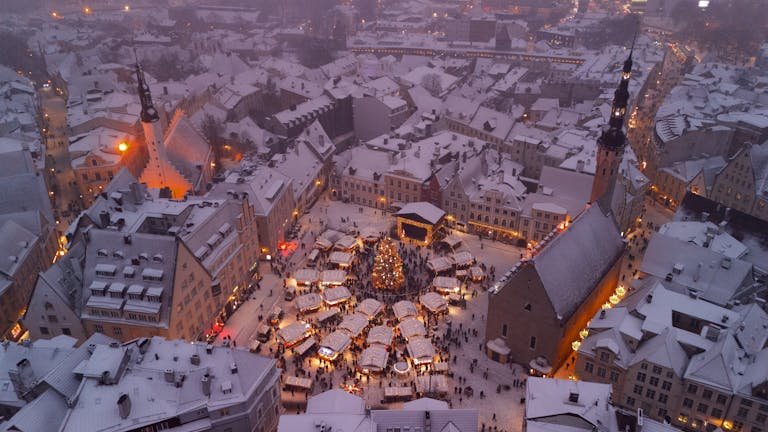 A scenic aerial shot of snowy Tallinn's Christmas market with twinkling lights at dusk.