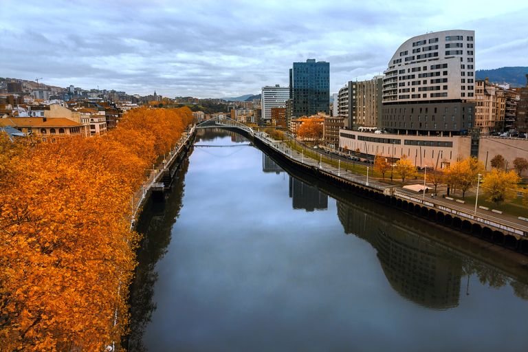 Autumn view of a river in Bilbao, Spain with orange foliage and modern skyline.