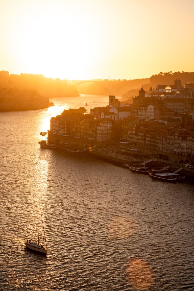 Stunning aerial view of Porto, Portugal during sunset with a river and sailboat in the frame.