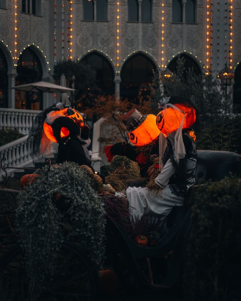 Spooky Halloween scene with people in costumes, featuring glowing jack-o'-lantern heads in an urban setting.